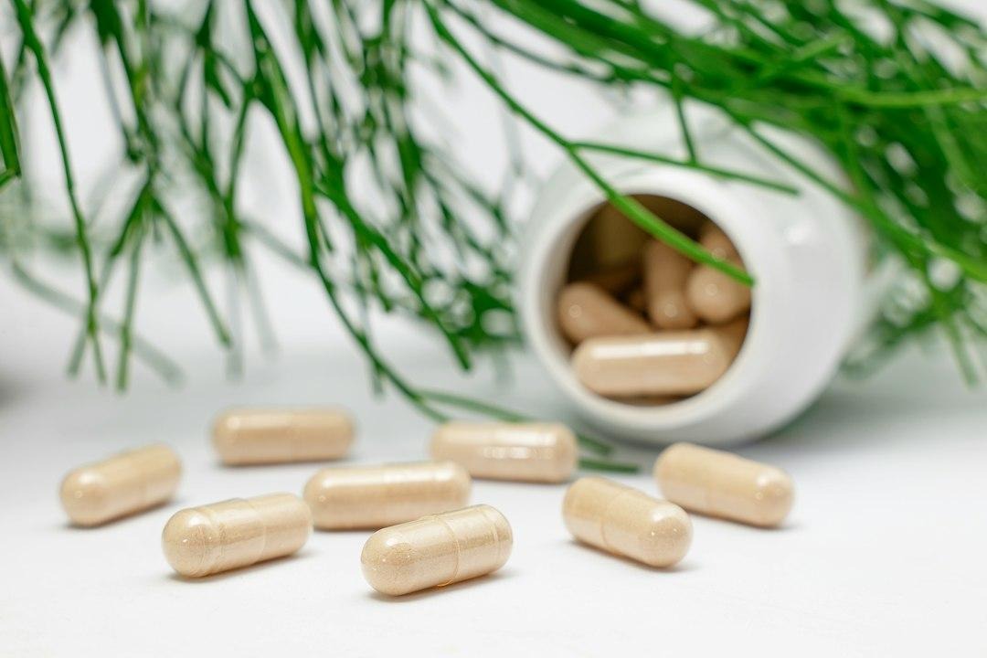 Beige powder-filled capsules spilling from a small white bottle onto a table